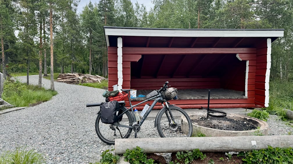 A black bike with a backpack on the back of it parked next to a red shed.