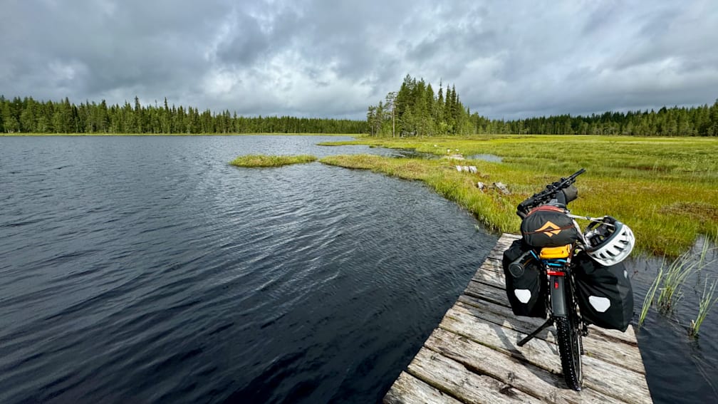 A docked boat is in front of a forest and next to a lake.