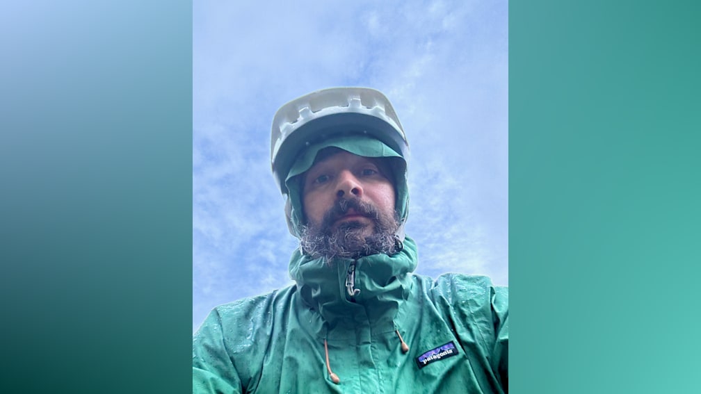 A man wearing a green Patagonia jacket looks up at the camera.