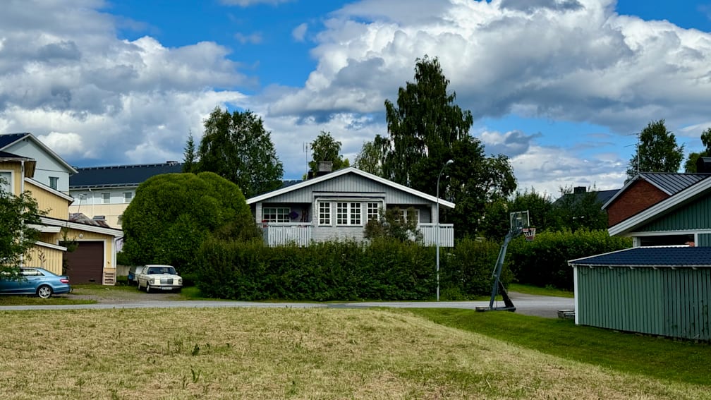 A house with a basketball hoop in front of it sits on a grassy lot.