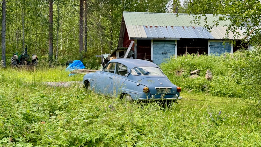 An old blue car is parked in a field with tall grass.