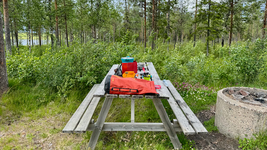 A picnic table with a red and orange bag on it in the middle of a field.