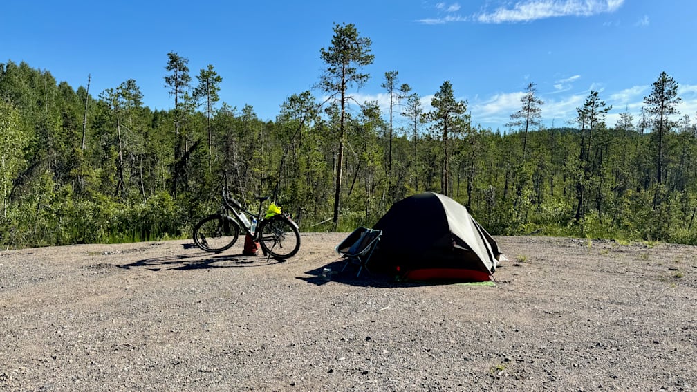 A bicycle is parked next to a tent in a wooded area.
