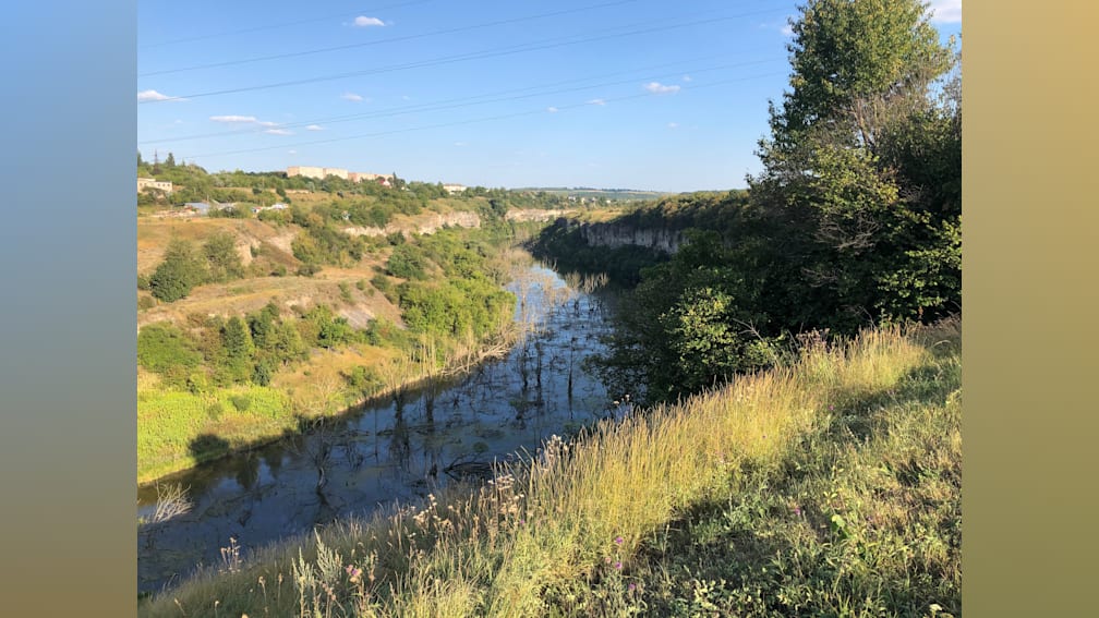 A river flows through a lush green countryside with trees in the background.