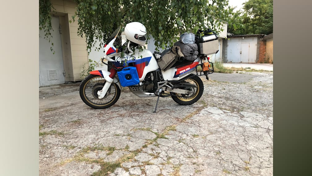 A red, white and blue motorcycle with a helmet on it in a driveway.
