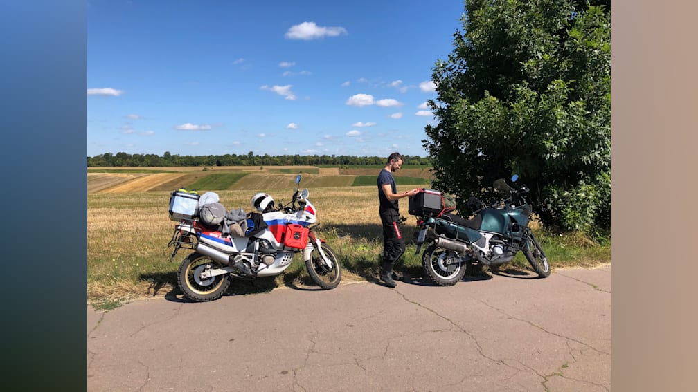 A man standing next to his motorcycle on the side of the road.