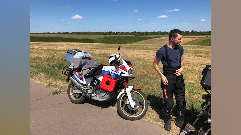 A man standing next to his motorcycle in a field.