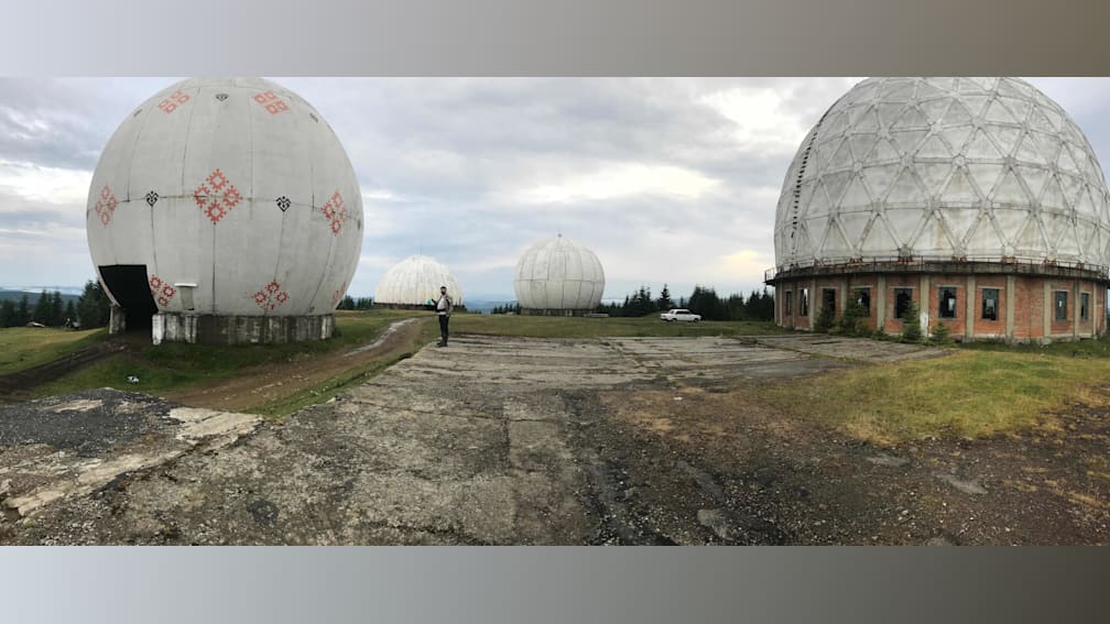 A man stands on a road near a set of domes, with a car in the background.