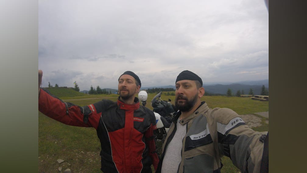 Two men wearing motorcycle gear taking a picture together.