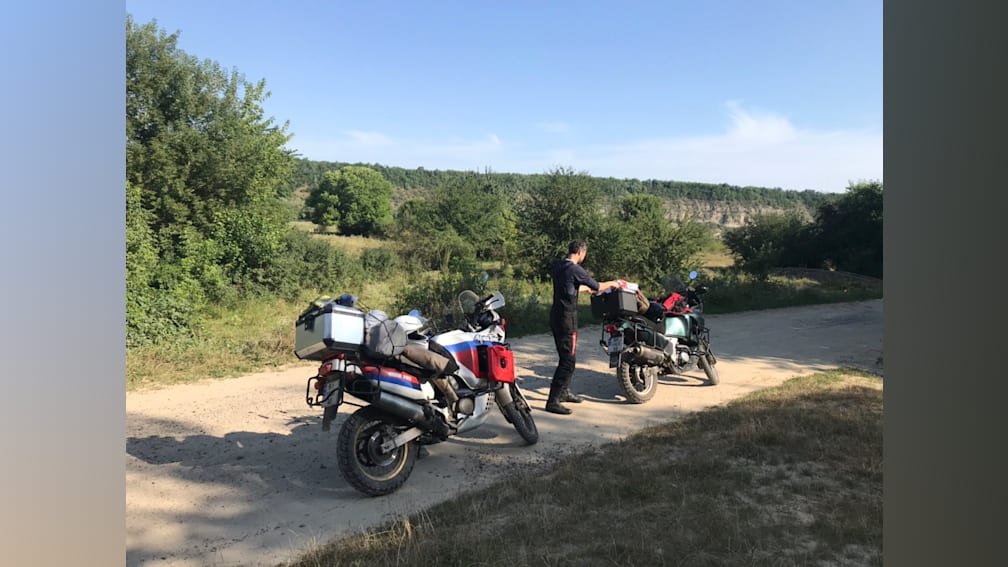 A man standing next to his motorcycle on a dirt road.