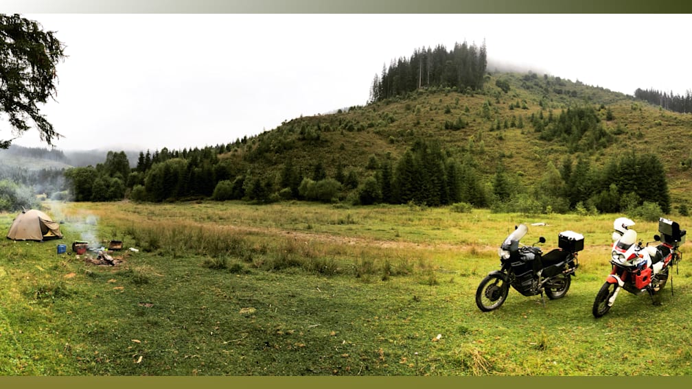 A black motorcycle is parked on a grassy field with trees in the background.