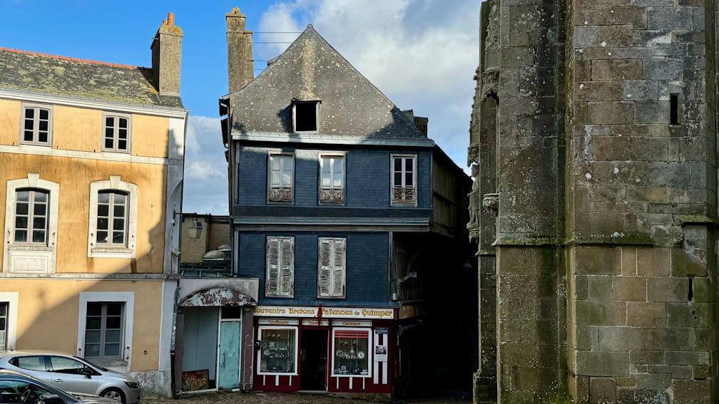A large, blue building with shutters on the windows sits next to a smaller building.