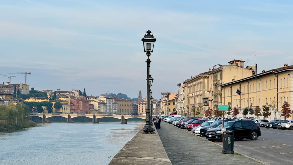 A street lamp on a sidewalk by the water with a bridge in the background.