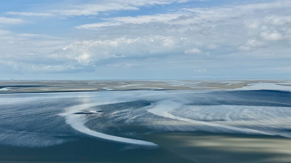 A blue sky and calm waters with no waves in sight.