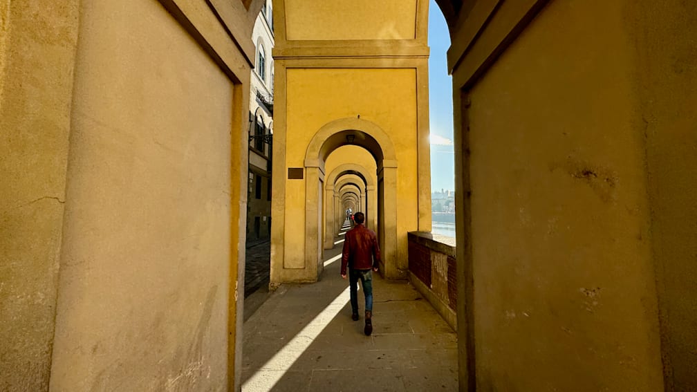 A man in a red jacket walks down a long hallway.