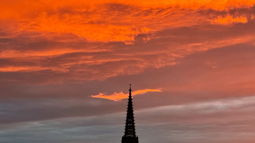 A tall tower with a pointy top and a dark silhouette against a pinkish sky.