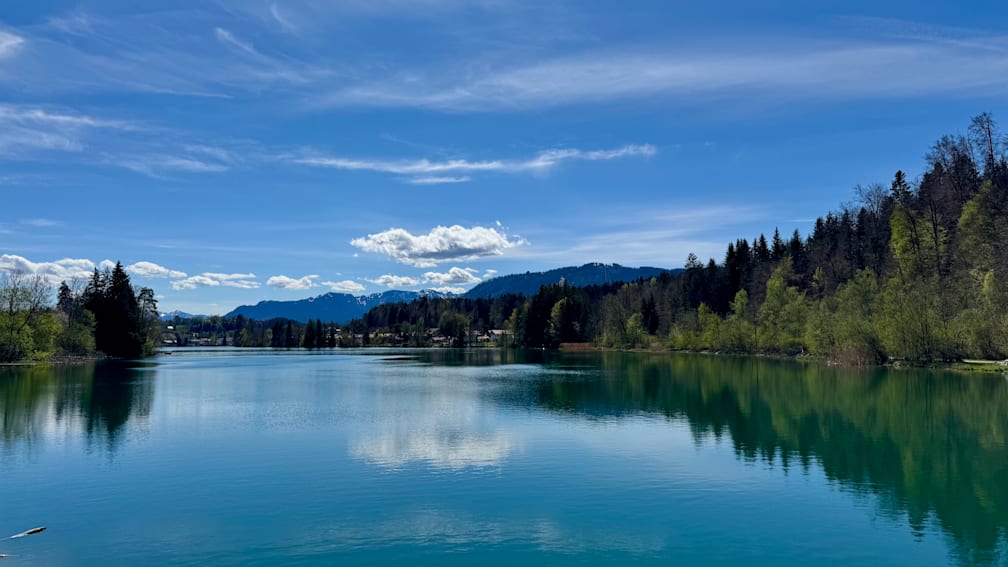 A lake is reflected in a clouded blue sky.