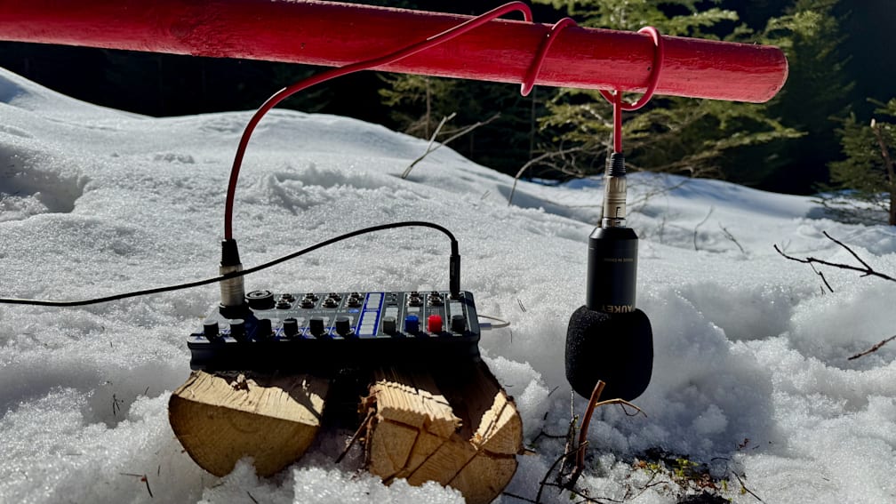 A remote control sits on a snowy log with a microphone attached to it.