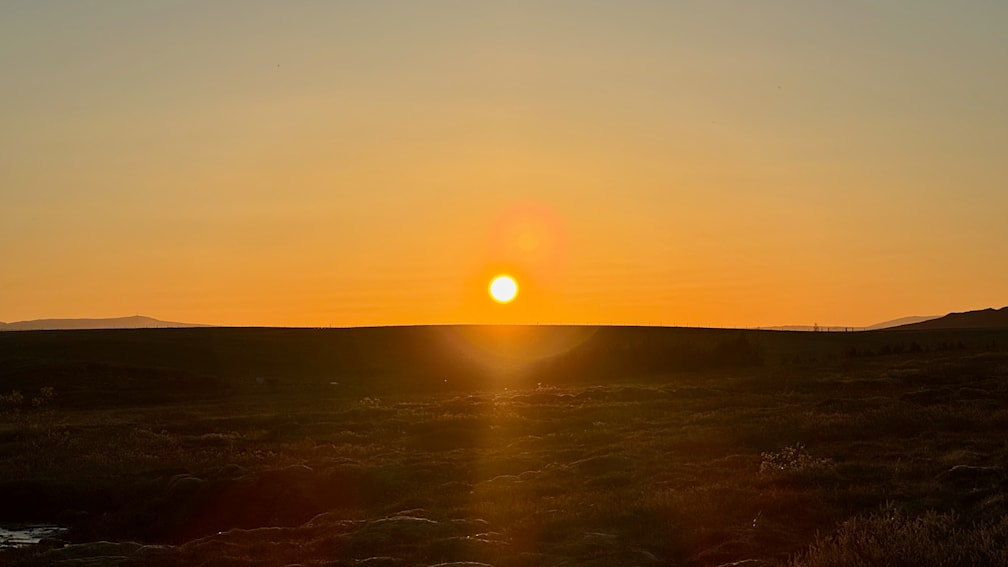 A sunset with a green and orange sky and small specks in the sand.