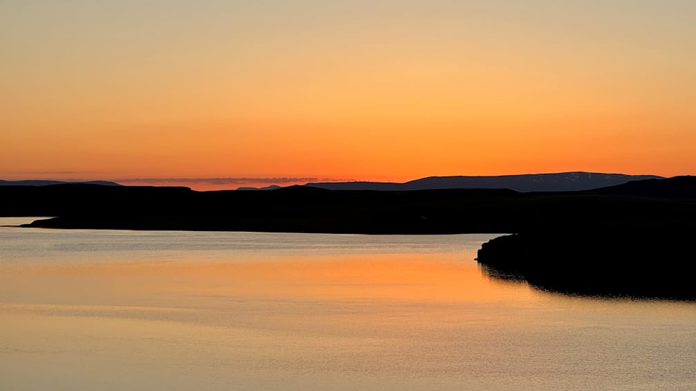 A sunset with a lake and mountains in the background.