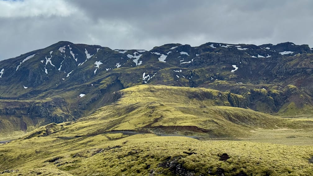 A mountain with a greenish yellowish tint to it and snow on it as well.