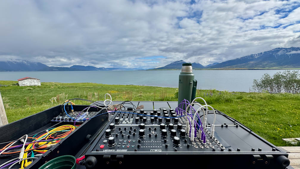 A black soundboard with several knobs and dials sitting on a table next to a green thermos.