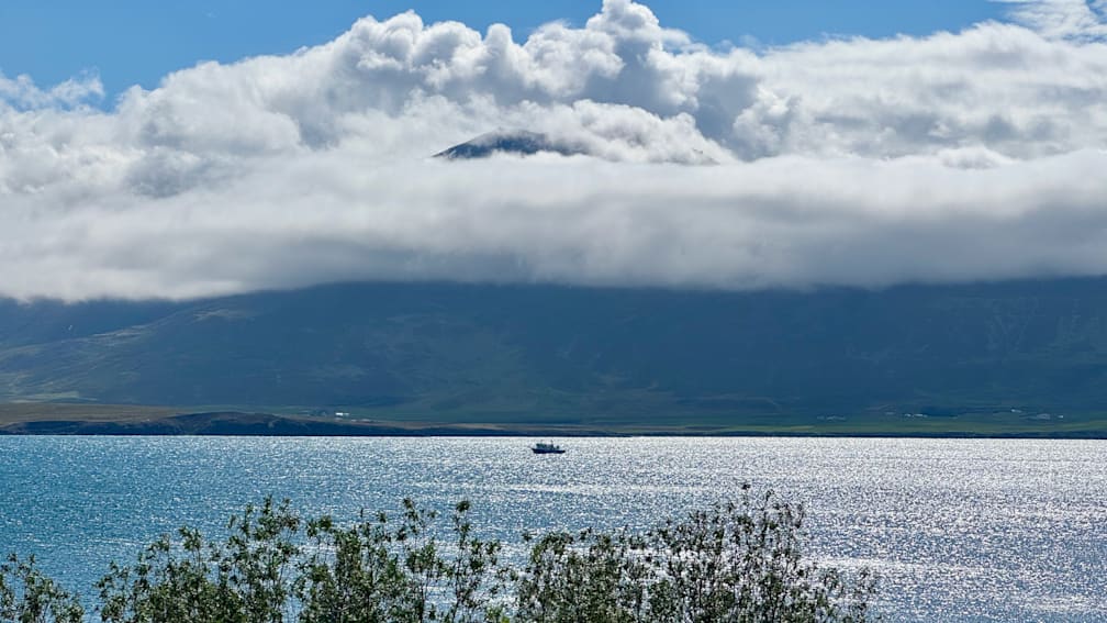 A boat can be seen on a cloudy day with a mountain in the background.
