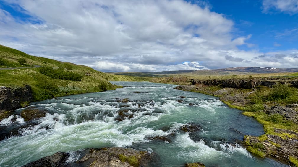 A picture of a river with a waterfall shown with clouds in the background.