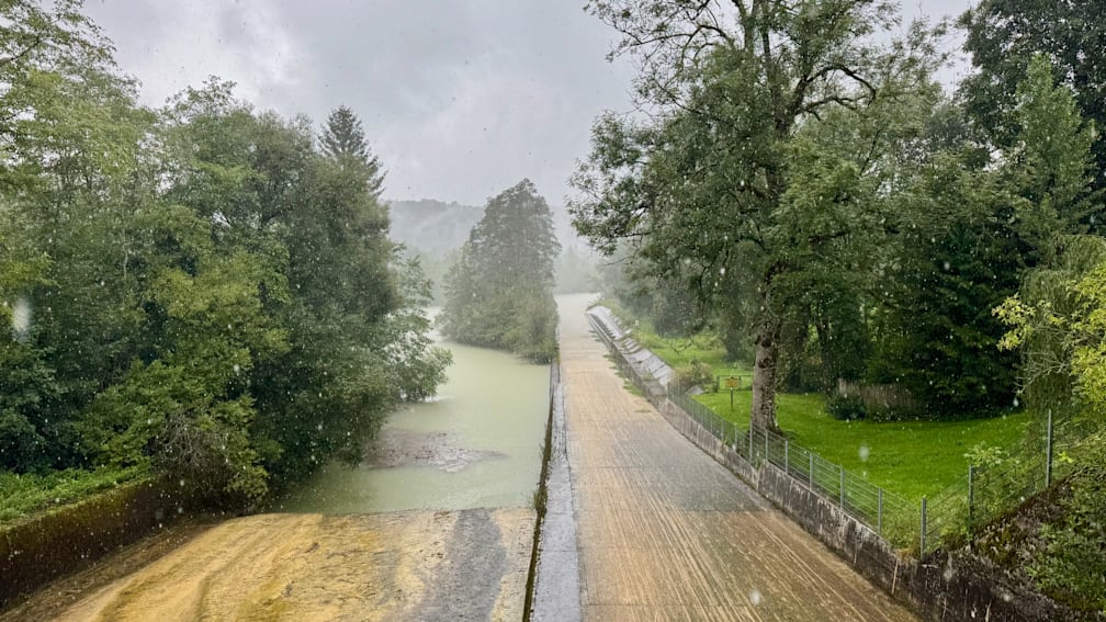 A road that is next to a river is very wet from the rain.