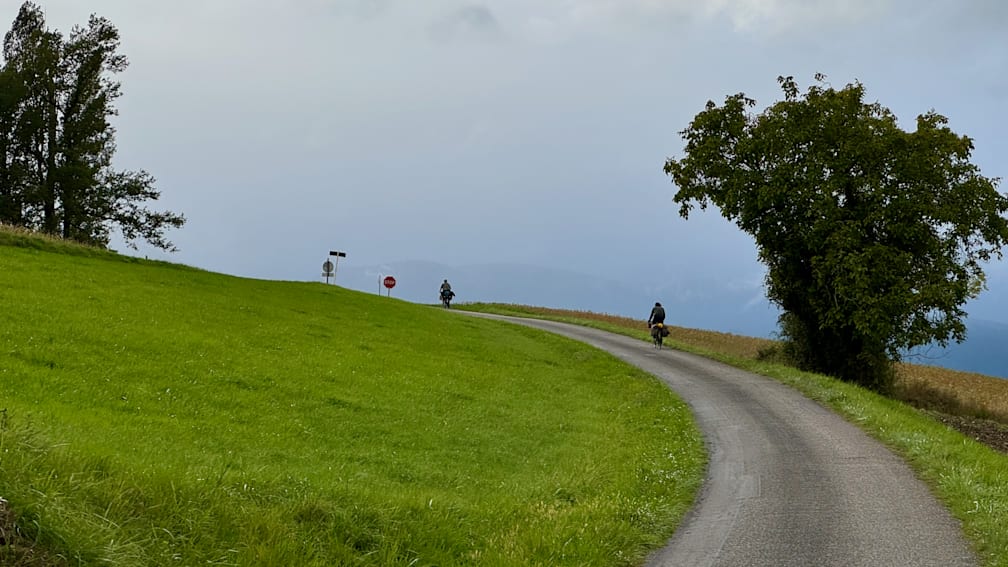 A road with a stop sign and two people on bikes going down the road.