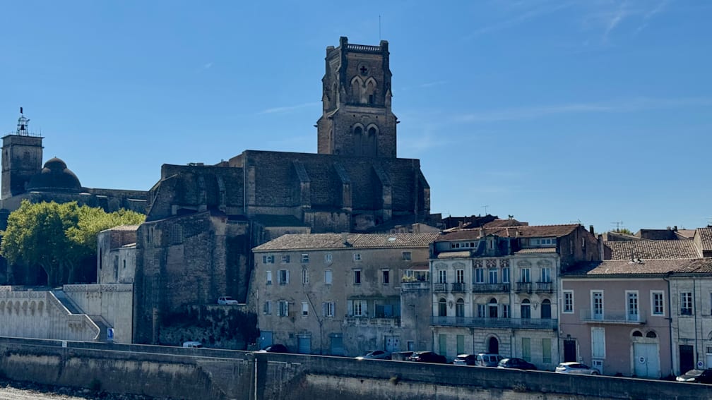 A building with a steeple and a group of multicolored birds flying by.