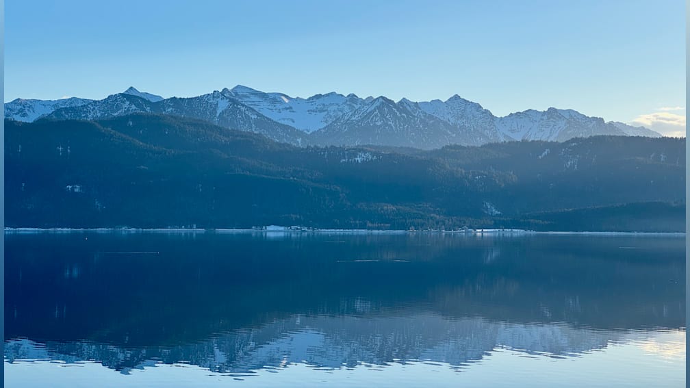 A mountain with a lake in front and a blue sky in the background.