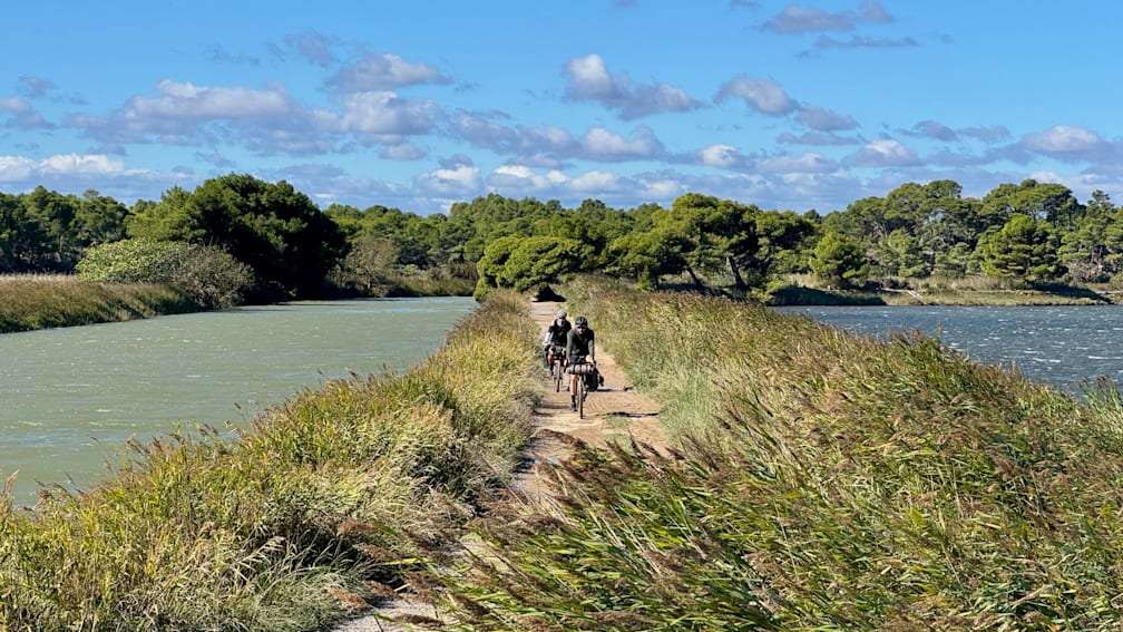 People on bikes are riding down a path next to a body of water.