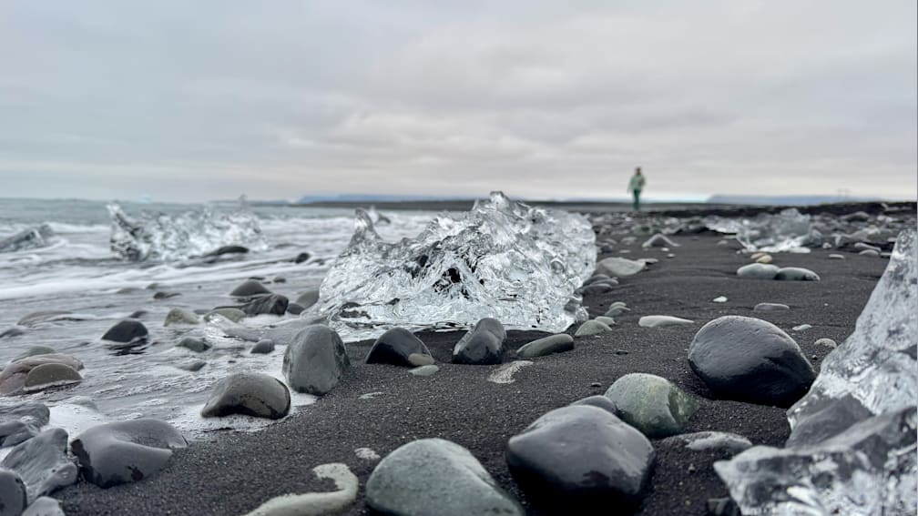 A person walking on a beach with large chunks of ice scattered around them.