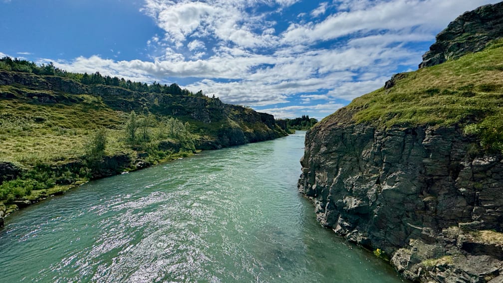 A river flows through a rocky canyon with a grassy bank on either side.