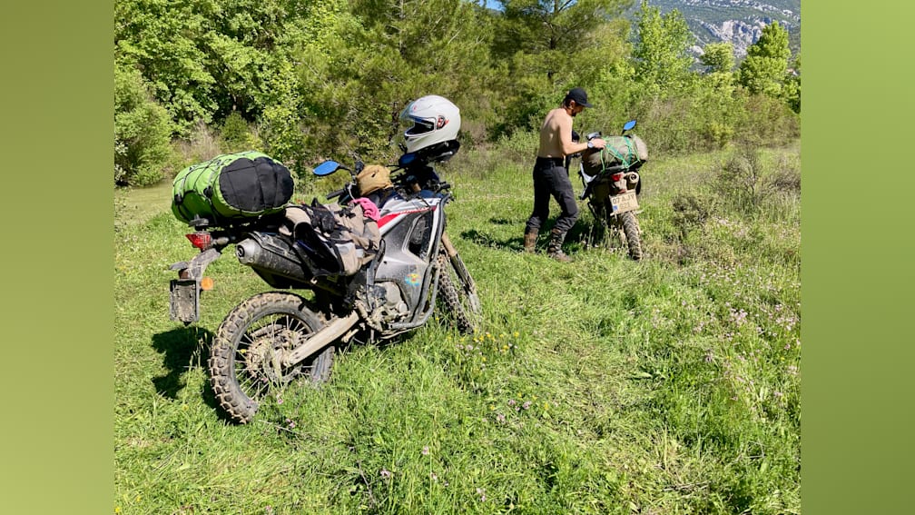 A man is sitting on a motorcycle in the grass with a white helmet on his head.