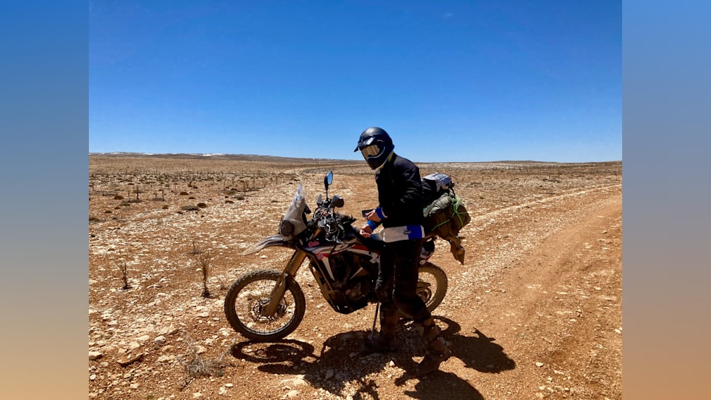 A man is standing next to his motorcycle in the middle of the desert.