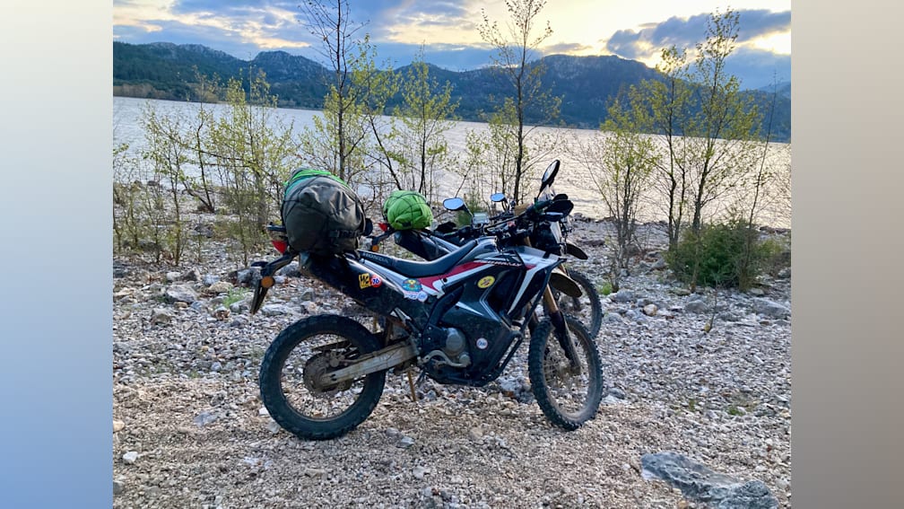 a motorcycle with a green bag on it next to a body of water.