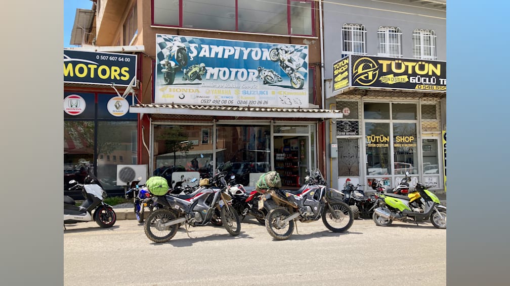 Several motorcycles are parked in front of a small store.