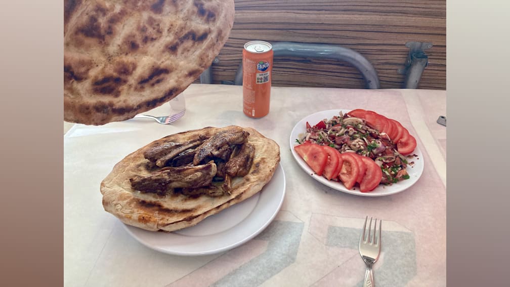 A plate of salad and a plate of meat are on a table with a can of soda between them.