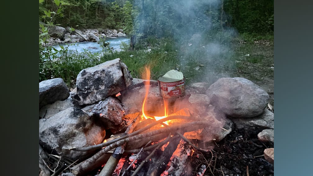 A fire is burning in a rock fireplace and a can of soup is sitting nearby.