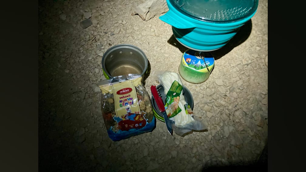 A small amount of food is sitting on a rocky ground next to a knife and a can of beans.