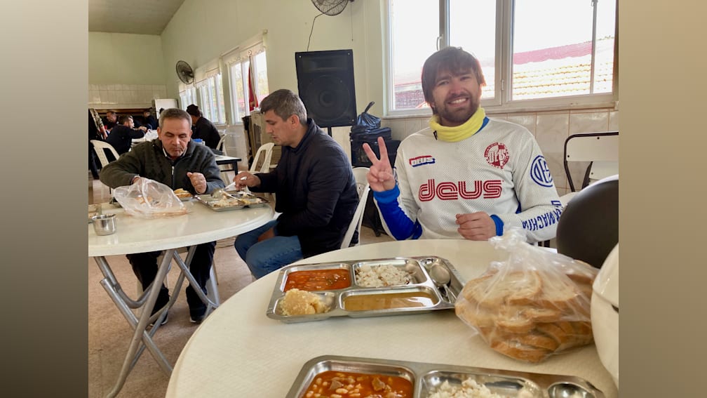 A man with a blue and white shirt that says Dues on it is sitting at a table with other people in a restaurant.