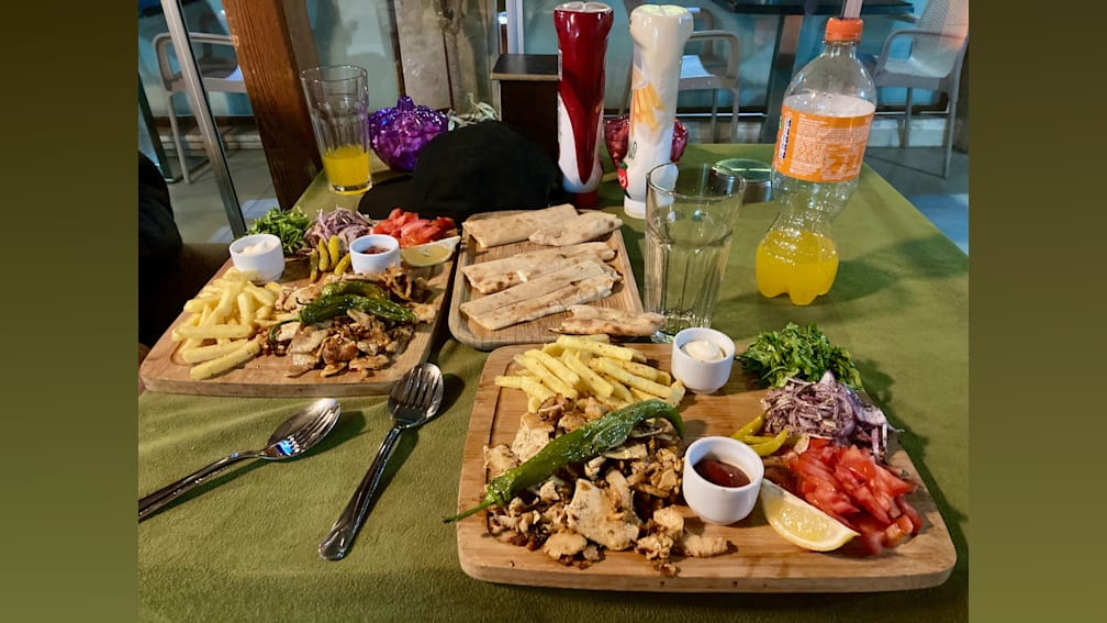 A table with two plates of food and two bottles of drinks.