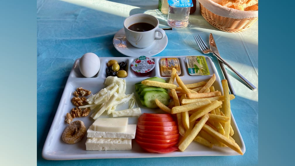 A breakfast plate with eggs, tomatoes, and cheese along with a side of fries and a drink.