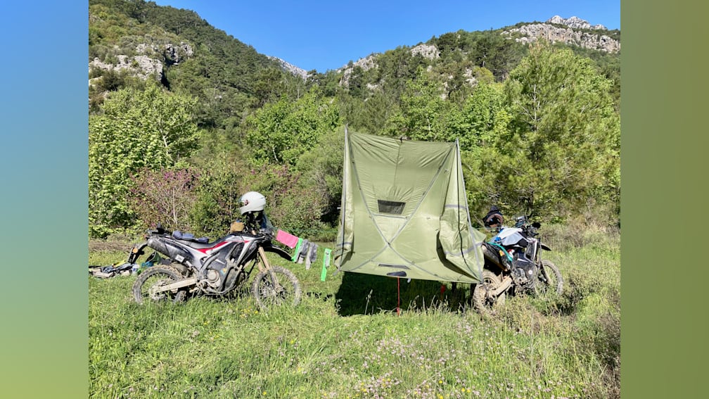 A green tent is set up next to a motorcycle on a grassy field.