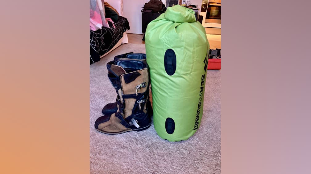 A pair of brown boots sits next to a green bag.