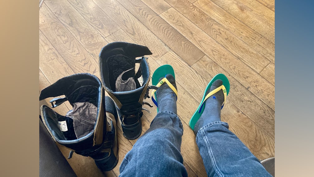Two people with flip flops and boots sitting on a floor.