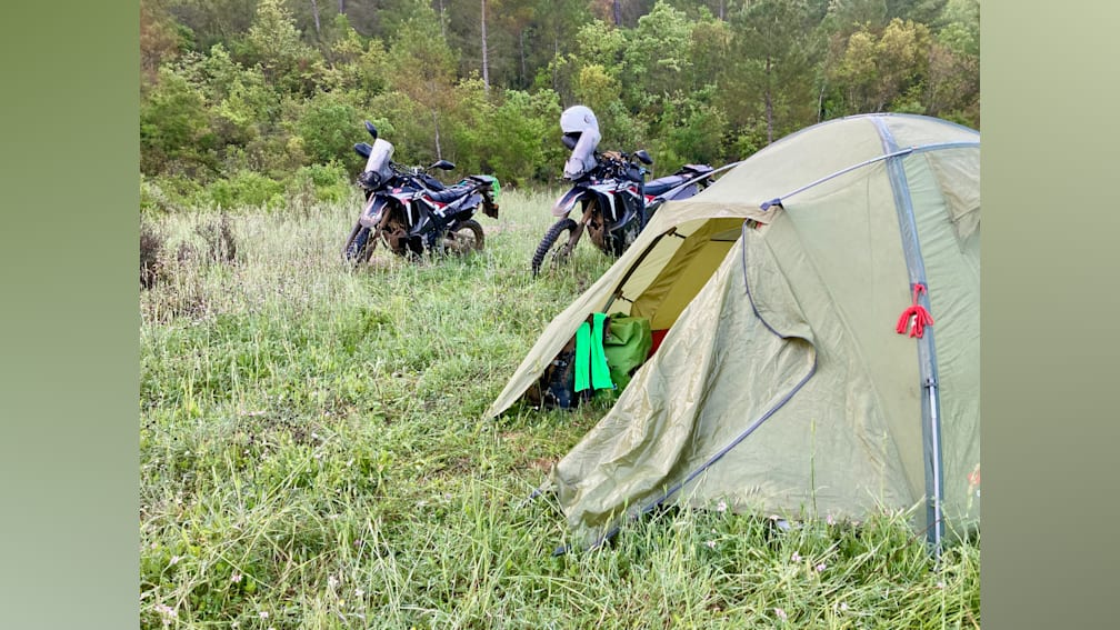 Two motorcycles are parked next to a tent on a grassy area.