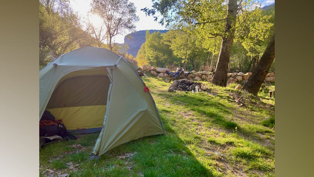 A tent is pitched in a grassy area with trees in the background.
